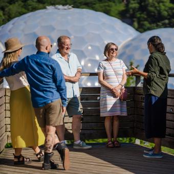 Eden tour guide introducing Eden to visitors on the viewing platform with Eden's Biomes in the background